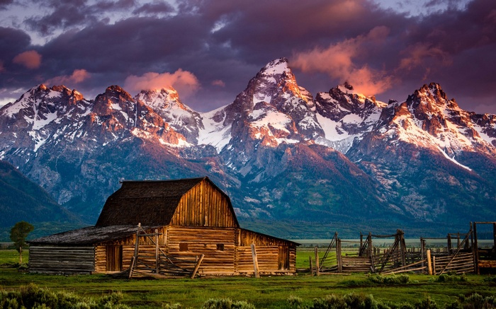 Wooden barn in front of snow-capped mountains at sunset