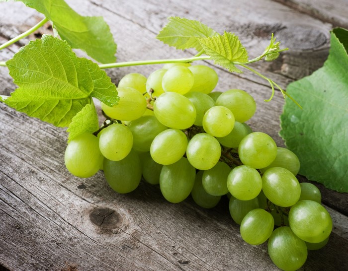 Green grapes with leaves on a wooden surface