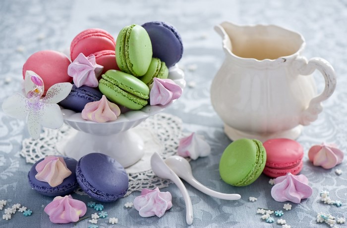 Colorful macarons and meringues on a white cake stand with a pitcher