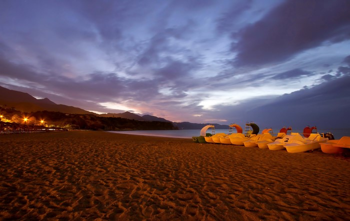 Pedal boats on a beach at dusk with mountains