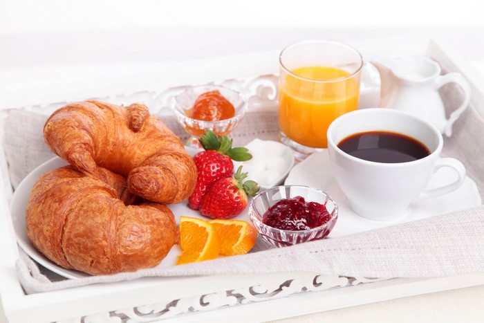 Breakfast tray with croissants, coffee, juice, and fruit