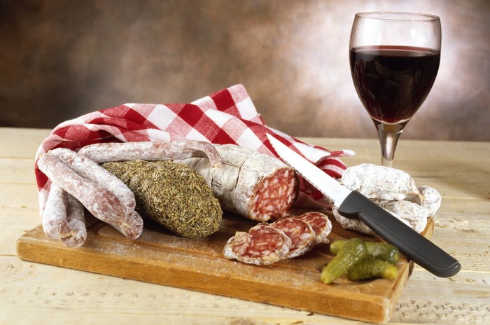 Still-life of sausages, pickles, knife, and red wine