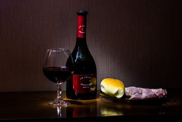 Still life with wine bottle, glass, bun, and ham