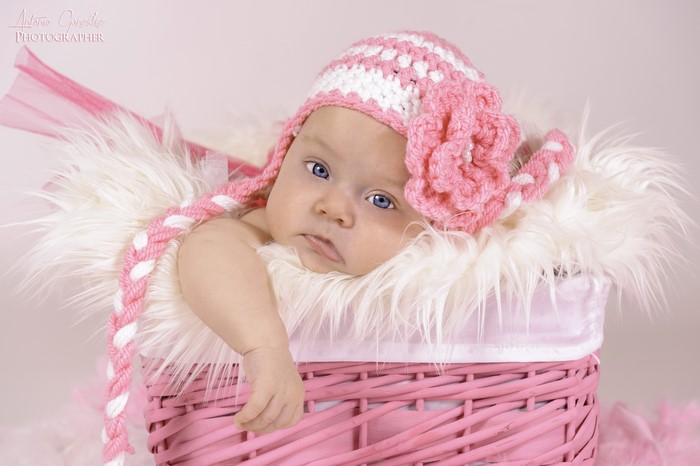 Baby in a pink and white crocheted hat in a wicker basket