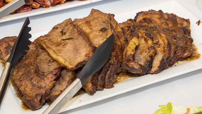 Sliced roasted meat on a platter with tongs