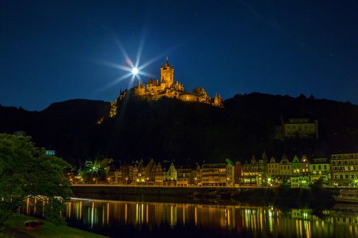 Cochem Castle illuminated at night with the moon over a river