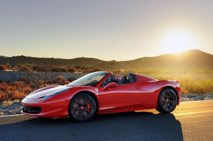 Red Ferrari 458 Spider convertible on a road at sunset