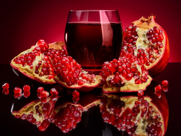 Pomegranate juice and fruit on a reflective surface