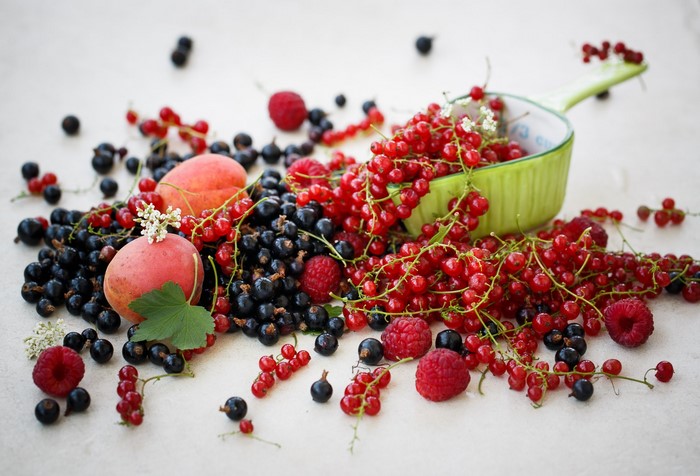Fresh berries and peaches spilling from a green bowl