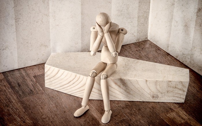Wooden mannequin sitting on a coffin