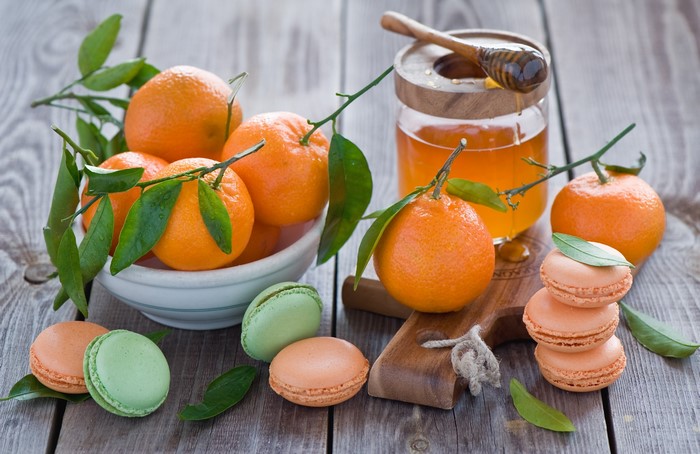 Tangerines with honey and macarons on a wooden table