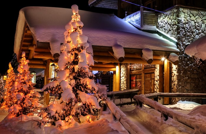 Snow-covered Christmas trees and log cabin at night