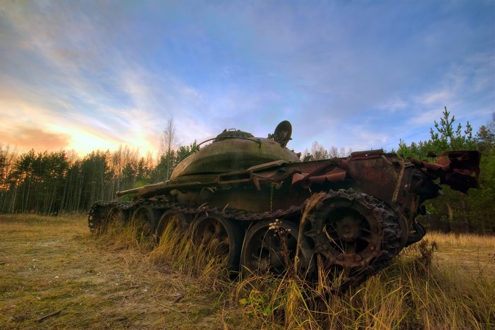 Abandoned rusty tank in a grassy field at sunset