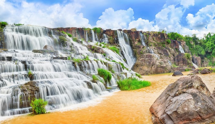 Multi-tiered waterfall cascading over rocks into a muddy river