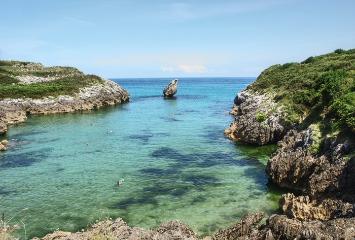 People swimming in a clear cove on the coast of Spain