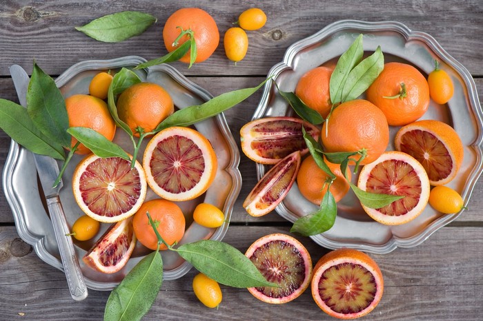 Blood oranges and kumquats on silver plates with a knife