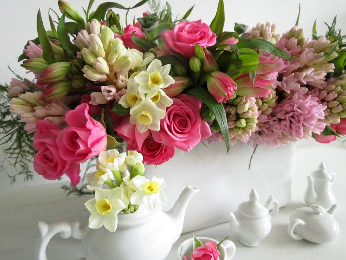 Pink roses, hyacinths, and daffodils in a bouquet with miniature teapots