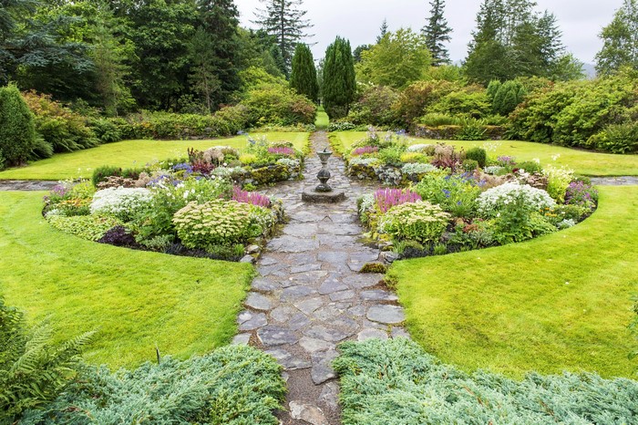 Stone path through a formal garden with flowers and trees