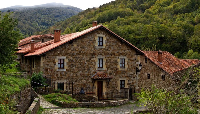 Stone houses with red tile roofs in a green mountainous landscape