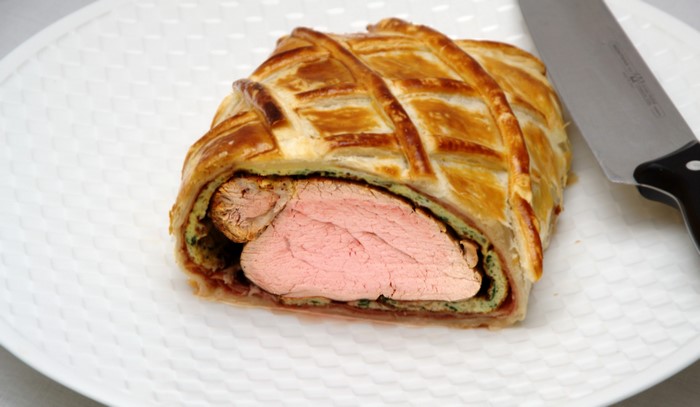 Beef Wellington on a white plate with a knife