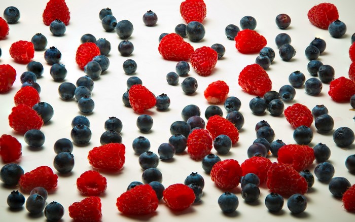 Raspberries and blueberries scattered on a white surface