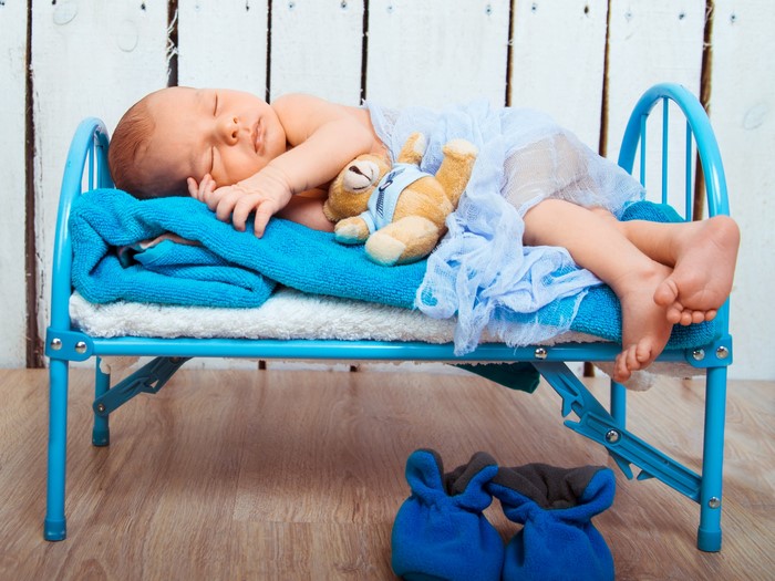 Baby sleeping with teddy bear on a blue bed