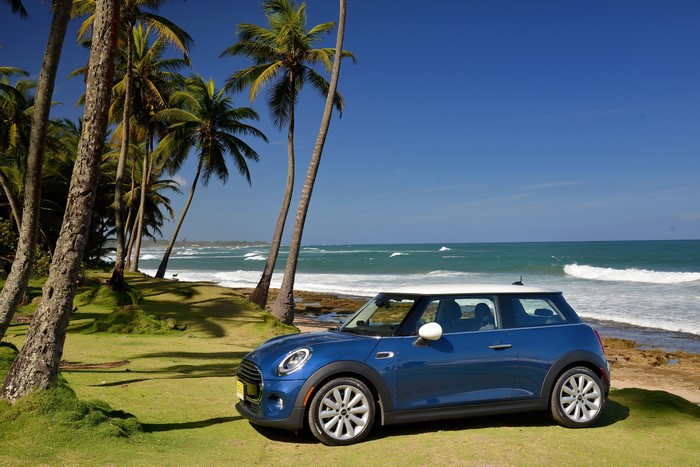 Blue Mini Cooper F56 parked by the ocean with palm trees