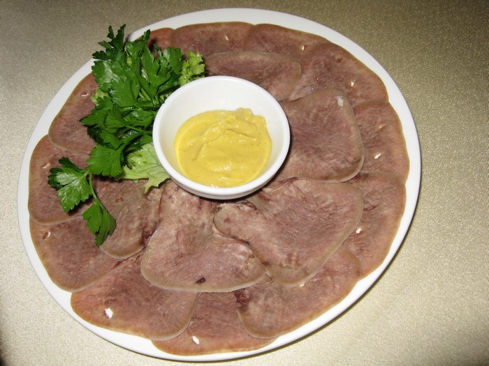 Sliced meat with mustard and parsley on a plate