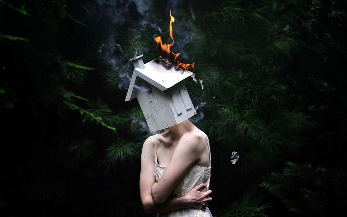 Woman with burning birdhouse on head in forest