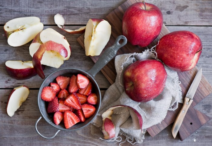Apples and sliced strawberries on a wooden table