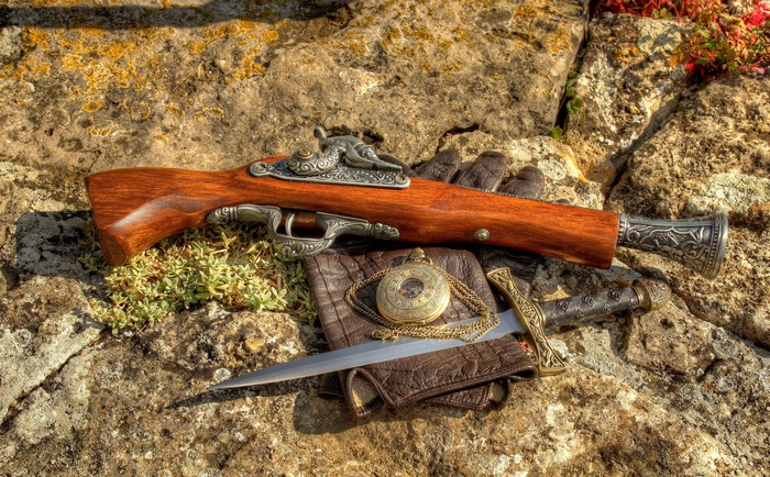 Flintlock pistol, dagger, pocket watch, and gloves on stones