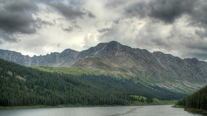Lake and mountains with pine forest under cloudy sky