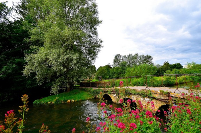 Stone bridge over a river in Bibury, England with trees and flowers