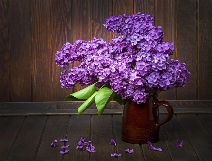 Lilac flowers in a brown jug on a wooden table