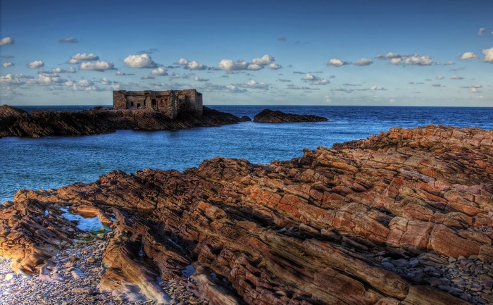 Ruined fortress on rocky coast with blue sea and clouds