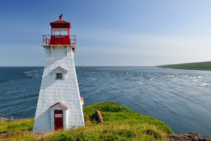 White lighthouse with red roof on a grassy cliff overlooking the sea in Tiverton, Nova Scotia