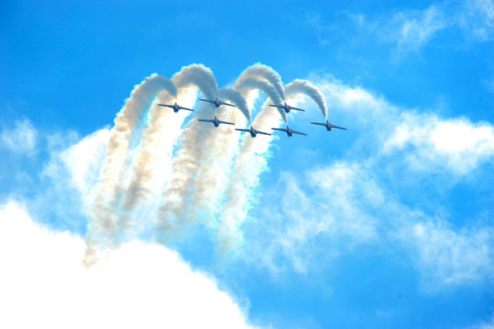 Seven fighter jets performing an aerial maneuver with smoke trails
