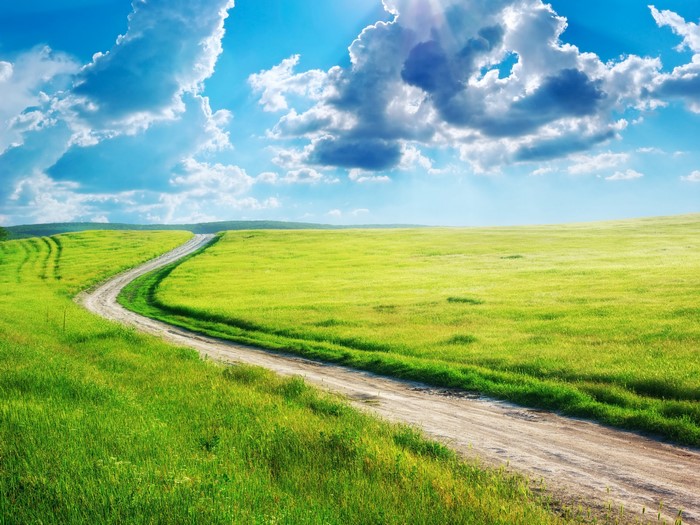Dirt Road Winding Through Green Fields Under Blue Sky