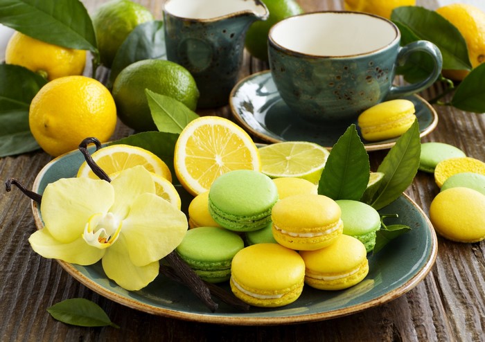 Yellow and green macarons with lemons, limes, orchid, and vanilla beans on a plate