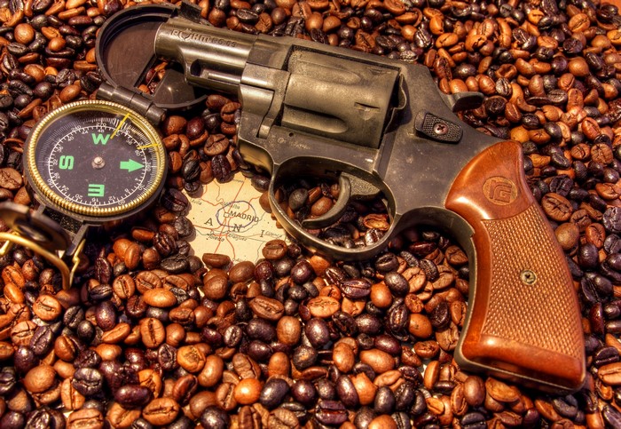 Revolver on coffee beans with compass and map