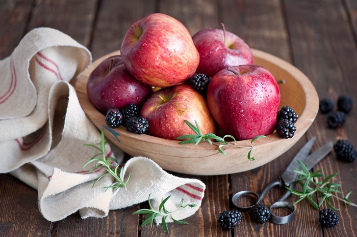 Apples and blackberries in a wooden bowl with rosemary