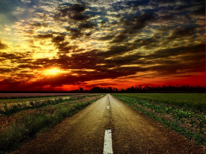 Road through fields at sunset with dramatic clouds