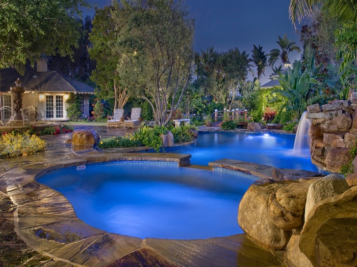 Luxury resort pool with waterfall and lounge chairs at night