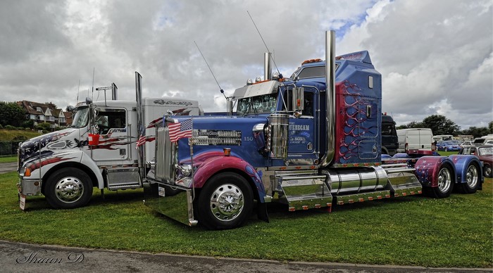 Two custom American flag themed Kenworth trucks parked on grass