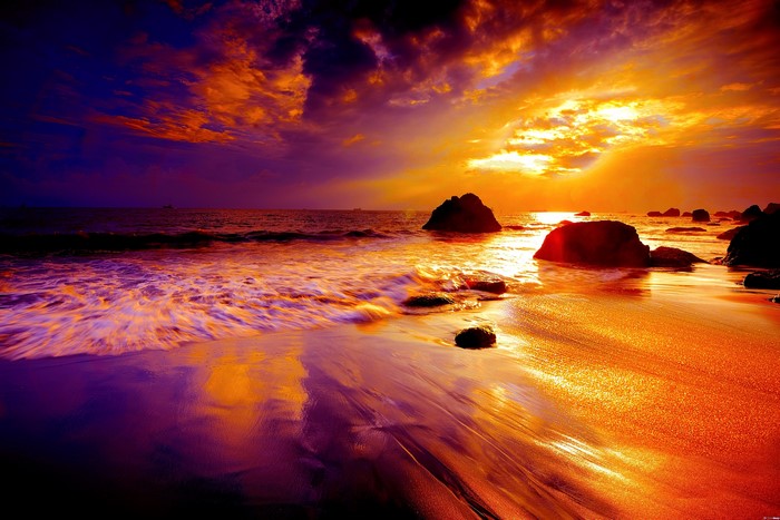 Sunset over the ocean with rocks on the beach