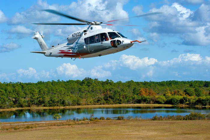 S-76D Helicopter flying over a lake and forest