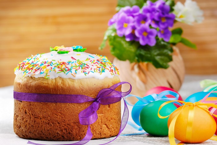 Easter Kulich with colorful sprinkles and ribbons, decorated eggs, and purple flowers