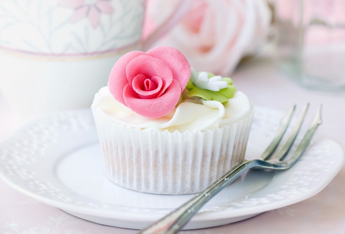 Cupcake with pink rose decoration on a plate with a fork