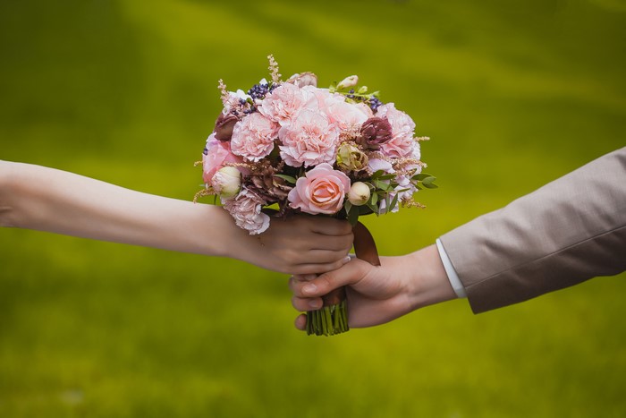 Two hands holding a bouquet of pink flowers