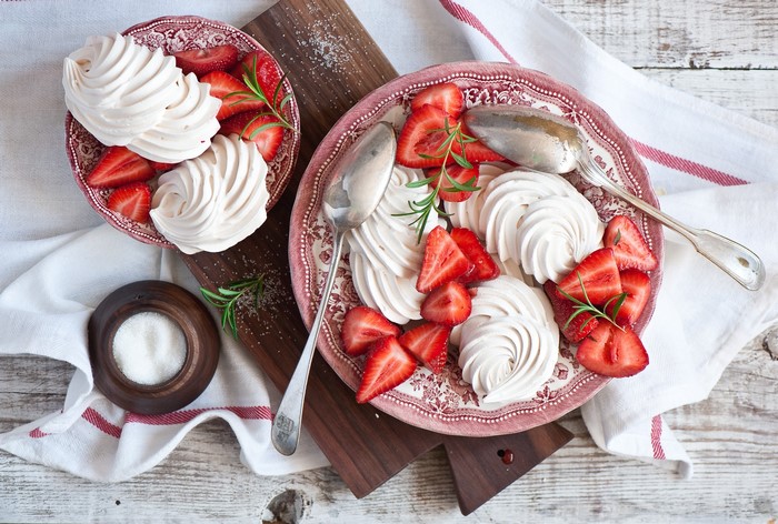Meringues with strawberries and rosemary on plates
